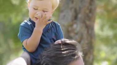Little boy sitting on the neck of his father and playing with his hair. Mid shot