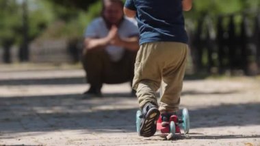 Küçük çocuk parkta scooterla babasına kayıyor. Orta çekim