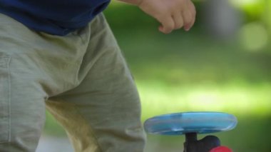 A little blonde boy spins a wheel on a childrens scooter. Mid shot