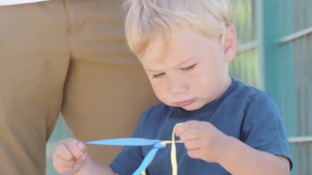 Маленький Хлопчик Язує Синьо Жовті Стрічки Середній Постріл — стокове відео