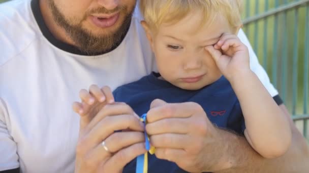 Little Boy His Father Ties Blue Yellow Ribbons Mid Shot — Vídeo de stock