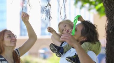 Genç bir aile parkta dikiliyordu. Küçük bir çocuk babasının omuzlarında oturuyordu. Orta çekim
