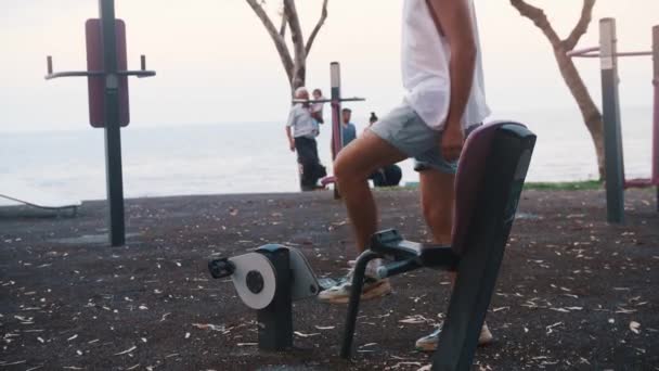 Young Man Sits Exercise Bike Beach Starts Training Mid Shot — Wideo stockowe