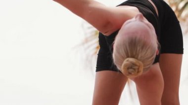 Sarışın bir kadın yoga minderinde vücudunu ısıtıyor. Orta çekim