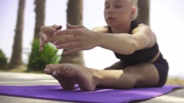 Deniz kenarında jimnastik - genç bir kadın yoga minderinde oturur ve ayakları üzerine eğilir. Orta çekim