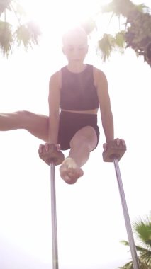 Gymnastics by the sea - a young blonde woman standing on the small high beams with her head upside down. Mid shot