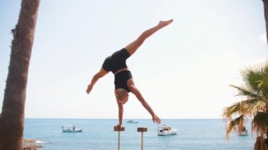 Gymnastics by the sea - a young woman doing a handstand on the high small beams. Mid shot