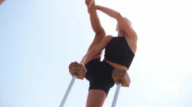 A young blonde woman doing gymnastic exercises by the high beams. Mid shot