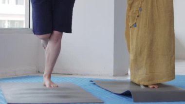 Three women doing yoga standing on mats. Mid shot