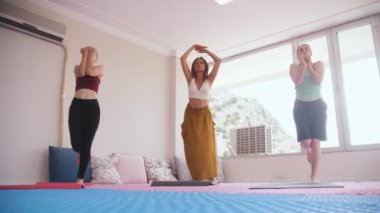 Yoga session - three women do yoga in a bright studio in daylight. Mid shot