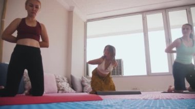 Three women do yoga - bending their faces to the floor taking the puppy posture. Mid shot
