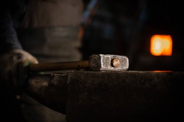 A hammer on the anvil in workshop - a man worker standing on the background. Mid shot
