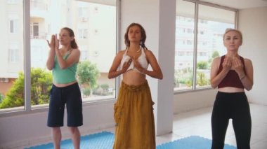 Three women standing in the bright studio and running their hands against their chests. Mid shot