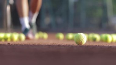 24-05-2022 TURKEY, ANTALYA: A young man walks around a court littered with tennis balls and picks up one of them. Mid shot