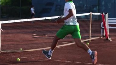 24-05-2022 TURKEY, ANTALYA: A young man player in sports uniform jumps over a net on a tennis court. Mid shot