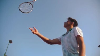 A young man tosses and catches tennis racket. . Mid shot