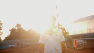 A young man tennisist walks to the camera in sunset light. Mid shot