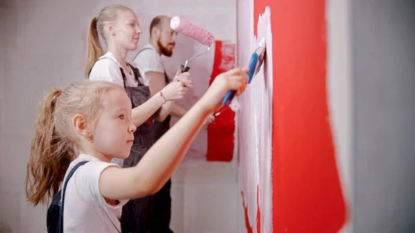 Family painting walls in red in the new apartment - a little girl painting wall with a brush. Mid shot