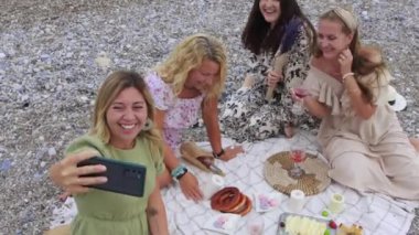 Four happy women taking selfie at the picnic on the beach. Mid shot