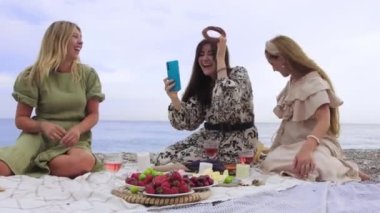 Funny women take selfies with bagels on the beach while having a picnic. Mid shot