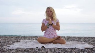 Woman in summer dress meditating by the sea. Mid shot