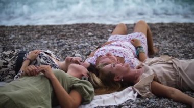 Four women lying on the blanket by the blue sea. Mid shot