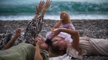 Four women lying on the blanket by the blue sea and looking at the sky. Mid shot