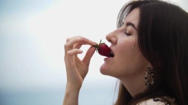 Adult brunette woman eating strawberry. Mid shot