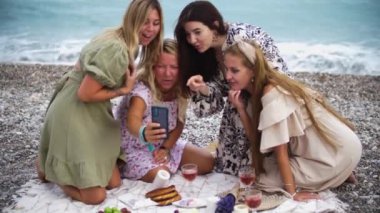 Four women having chilling on the beach - looking at the pictures on the phone. Mid shot