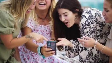 Four women looking at the pictures on the phone. Mid shot