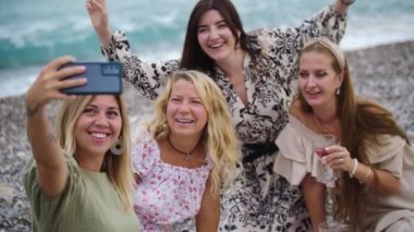 Four happy women taking a selfie on the pebble beach. Mid shot