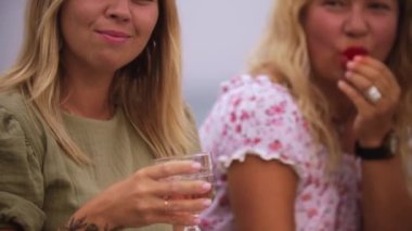 Four women drinking wine by the sea. Mid shot