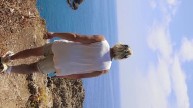 A man running to the cliff edge and spreading his hands. Mid shot