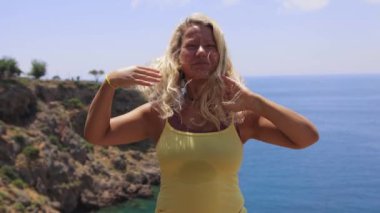 An adult smiling woman on the cliff edge by the sea. Mid shot