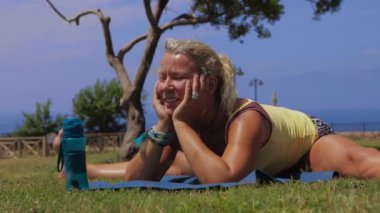 An adult woman doing yoga on nature - sitting on splits on yoga mat. Mid shot