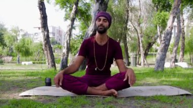 Smiling arabian man sitting on yoga mat in the park. Mid shot