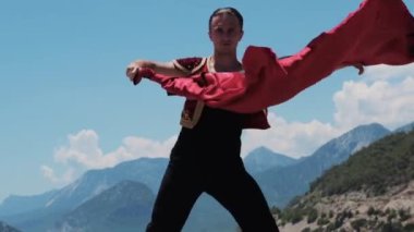 Sahne kostümlü çekici bir adam, güzel dağların yakınındaki plajda gösterisini sergiliyor. Orta çekim