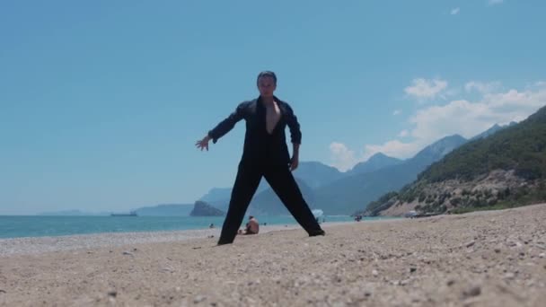 Seorang Pria Yang Menarik Dalam Kemeja Hitam Menari Tepi Laut — Stok Video