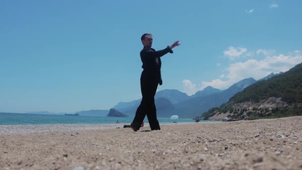 ビーチで優雅に踊る黒いシャツの魅力的な男 ミッドショット — ストック動画