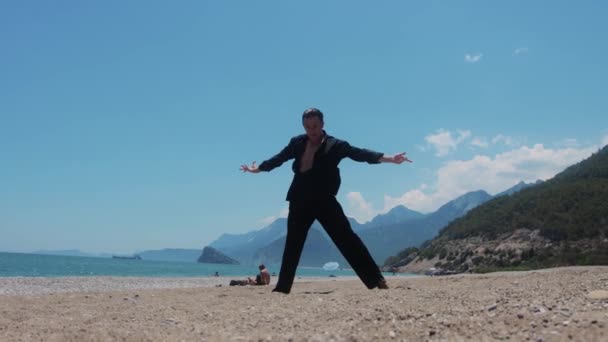 Een Aantrekkelijke Man Zwarte Kleren Dansend Het Strand Tussenschot — Stockvideo
