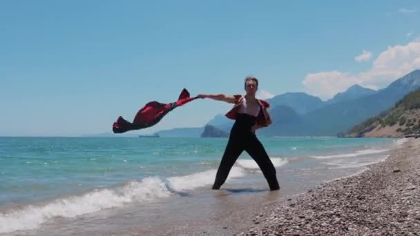 迷人的男舞者在海滨挥舞着一件红色斗篷 — 图库视频影像
