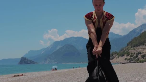 山の近くのビーチで彼の熱いパフォーマンスを示す舞台衣装の魅力的な男 ミッドショット — ストック動画