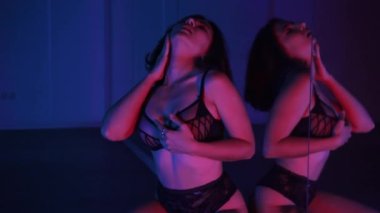 Siyah iç çamaşırlı seksi esmer ayna önünde neon ışıkta dans ediyor. Orta çekim