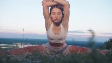 Akşamın erken saatlerinde yogada egzersiz yapan bir kadın öne doğru eğiliyor. Orta çekim