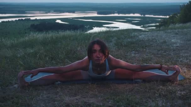 一个苗条的女人坐在山上的一个瑜伽垫上的裂缝上 向前倾斜着 — 图库视频影像