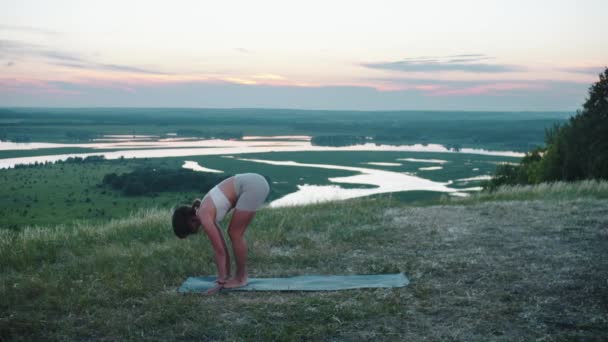 丘の上のヨガ 早い日没のヨガマットで練習をしている女性 ミッドショット — ストック動画