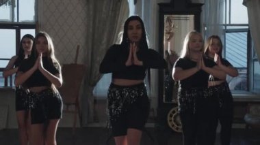 Bir grup kız ve dans eğitmenleri stüdyoda oryantal danslar yapıyorlar. Orta çekim