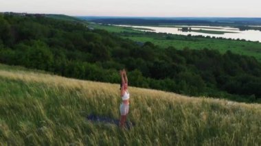 Yeşil alanda spor egzersizleri yapan bir kadın yoga minderinin üzerinde duruyor. Hava görünümü