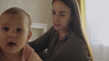 Anne ve küçük kızı birlikte vakit geçiriyorlar. Bebek yatakta kameraya doğru emekliyor. Orta çekim