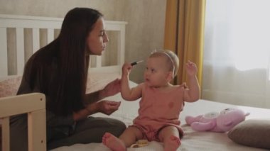 Bir anne küçük kızıyla oynar. Bir bebek annesinin yüzüne merhem sürer. Orta çekim